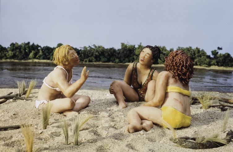Photograph of three figures made in clay sitting on a beach