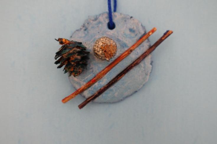 Clay mobile with two sticks, an acorn, and pinecone.