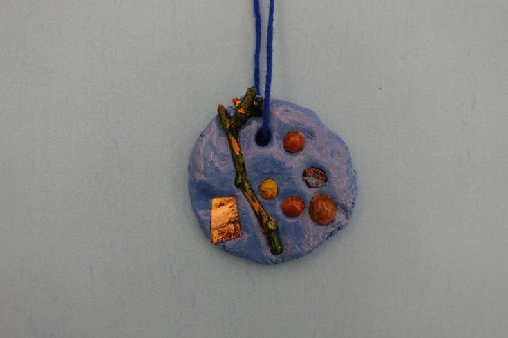 Clay mobile with painted holly and a stick.