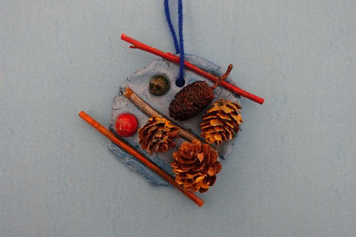 Clay mobile with sticks and painted pinecones.
