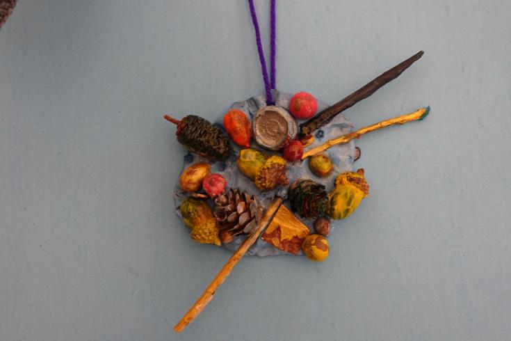 Clay mobile with painted sticks, acorns, and pinecones.