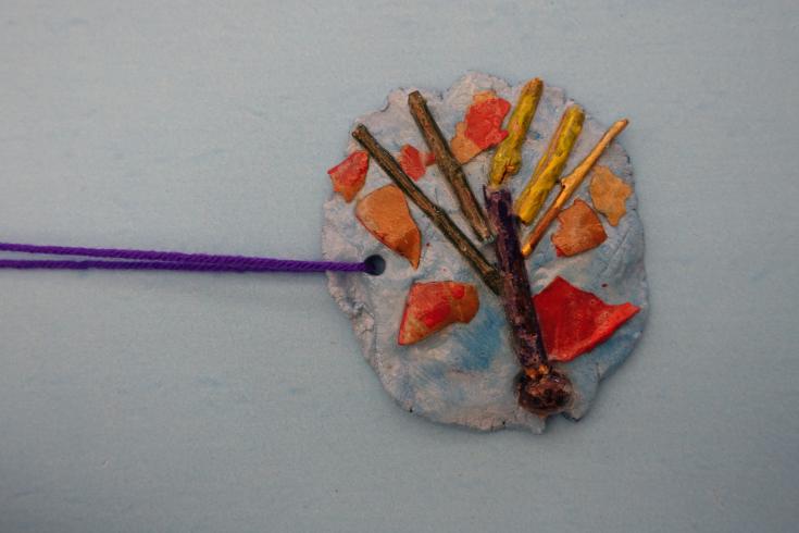 Clay mobile with painted sticks and wood chips.