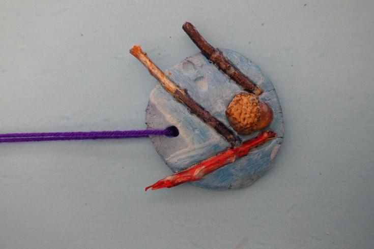 Clay mobile with painted sticks and an acorn.