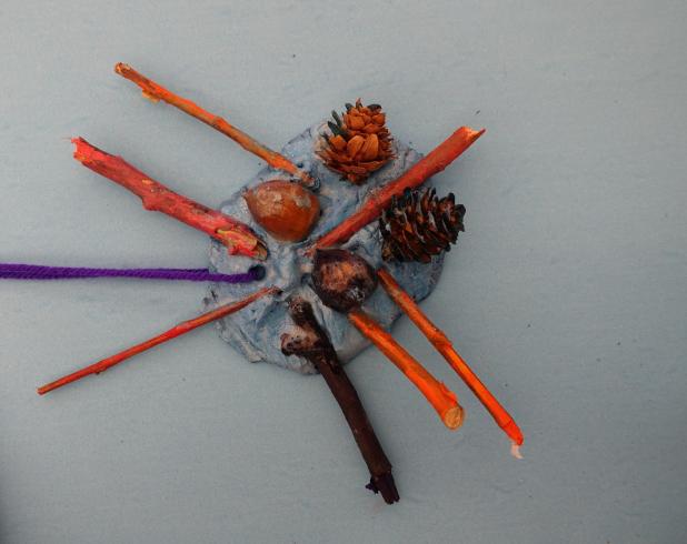 Clay mobile with painted sticks, acorns, and pinecones.