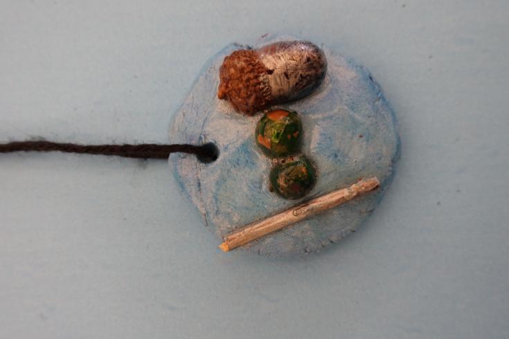 Clay mobile with painted acorns and a stick.