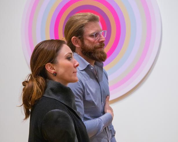 Photograph of two people looking off to the right, standing in front of a circular pink painting