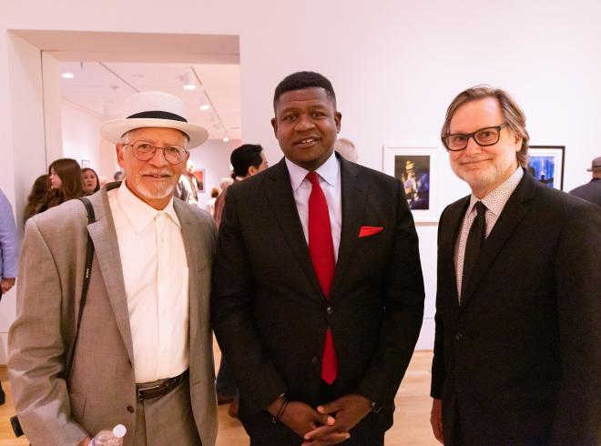 Three men in suits standing together in the galleries smiling at camera