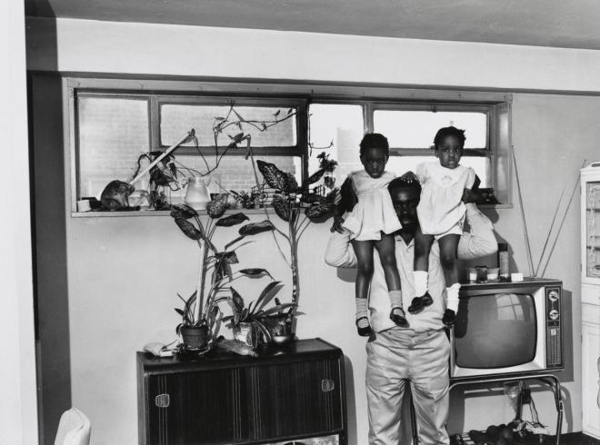 Black and white photograph of Black man with two little Black girls on his shoulders