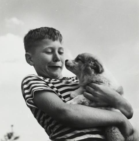 Black and white photograph of white boy in striped shirt hugging a puppy