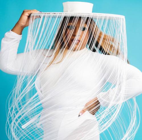 Headshot of Baddie Brooks in a white hat with long tendrils