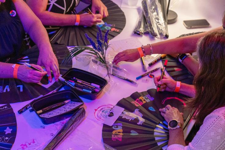 Overhead photograph of people decorating black fans with markers and other art supplies