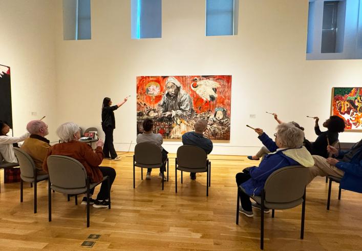 A group of people sitting listing to an educator talk about an artwork 