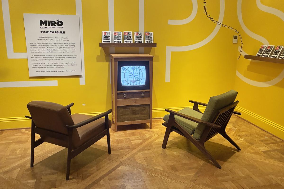 Two chairs in front of a retro tv against a yellow wall 