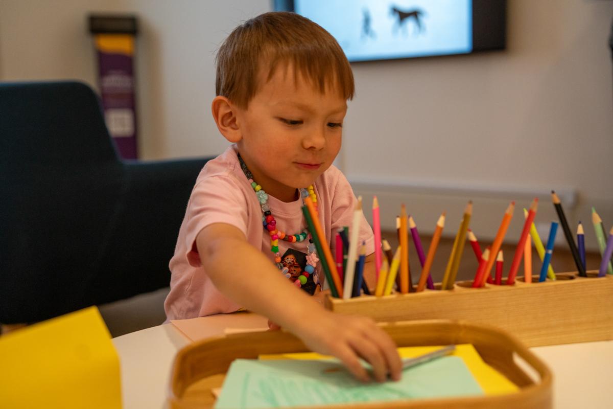 A kid sitting at a table with paper and color pencils
