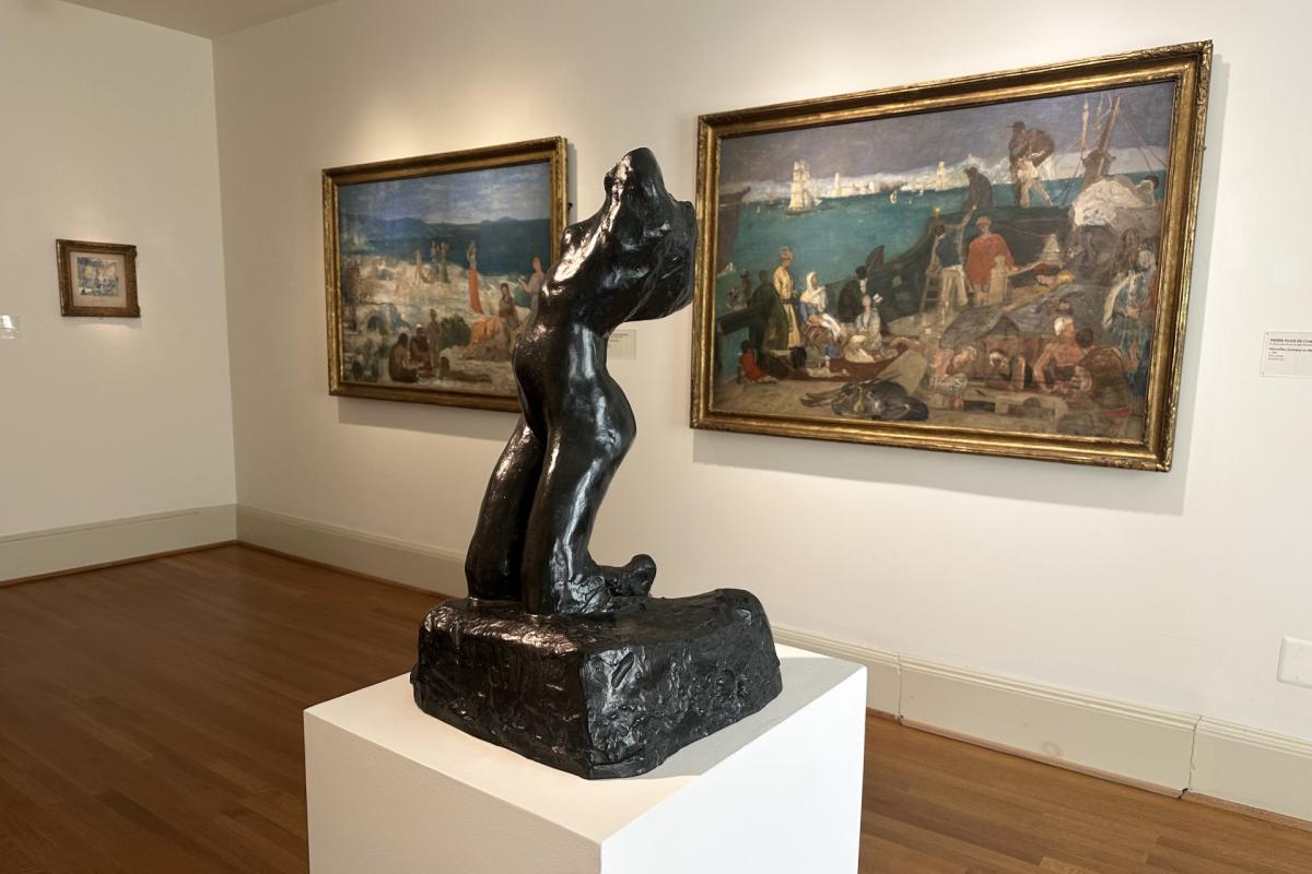 Three paintings on display in a gallery with a sculpture in the center of the room